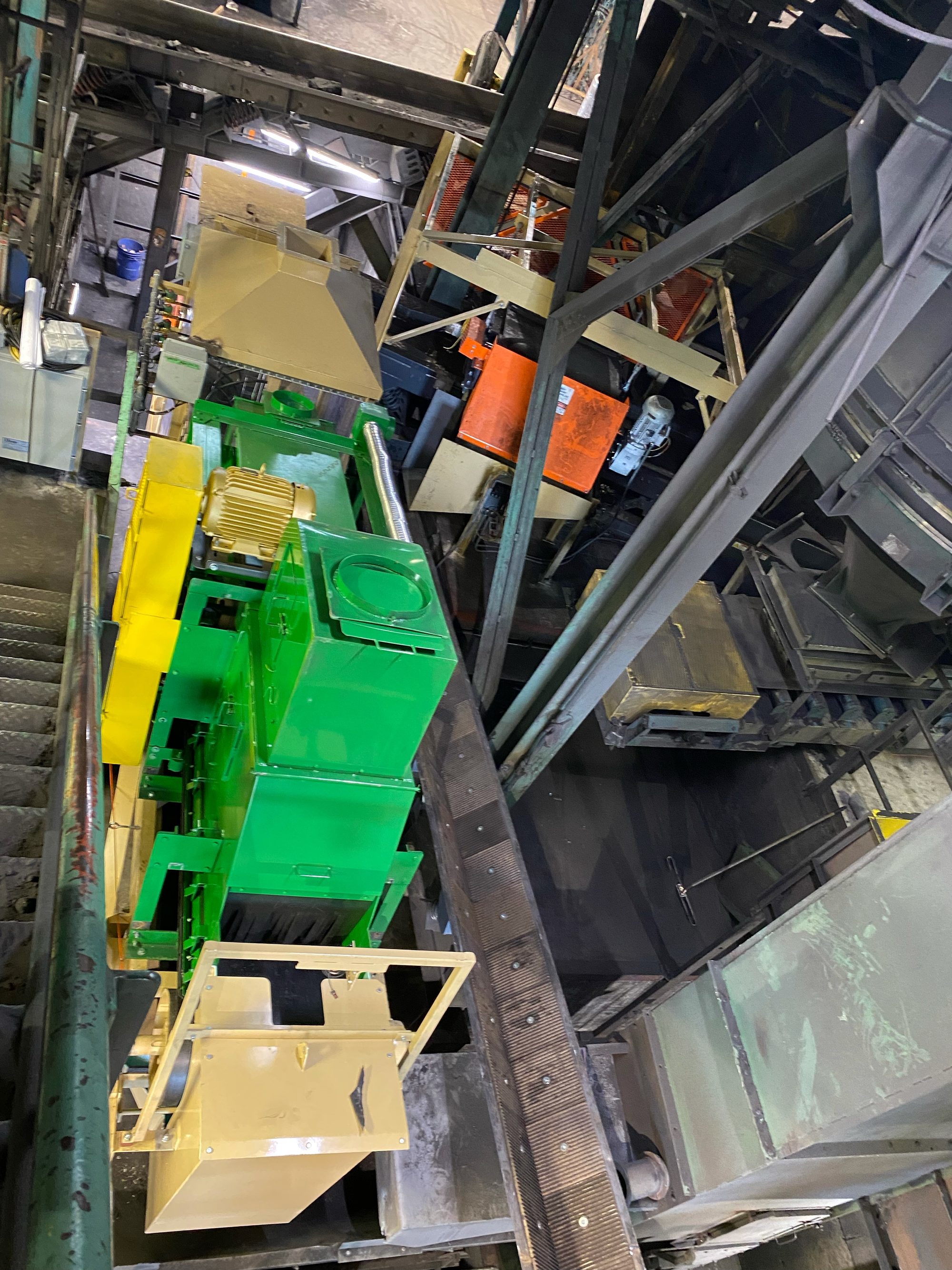 Green and yellow sand reclaim equipment mounted above a belt conveyor in a foundry